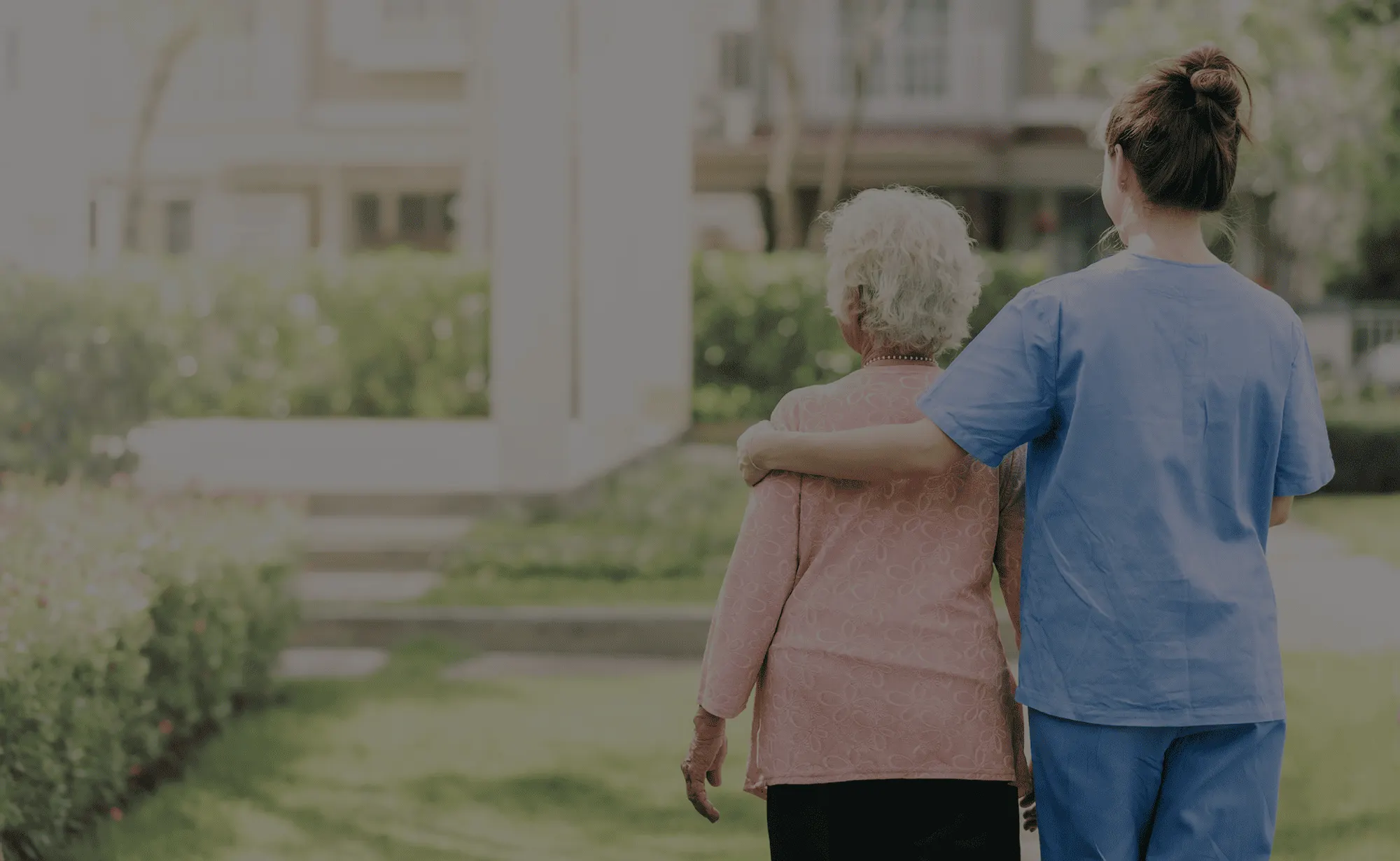 Pflegerin begleitet eine Seniorin bei einem Spaziergang im Grünen